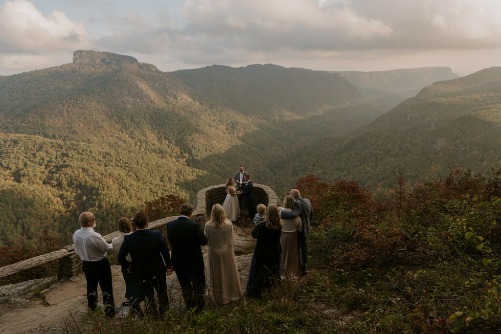 An elopement ceremony with family in front of a big mountain scene in the late afternoon. The couple stands with an officiant in a rock outcropping while the people look on.