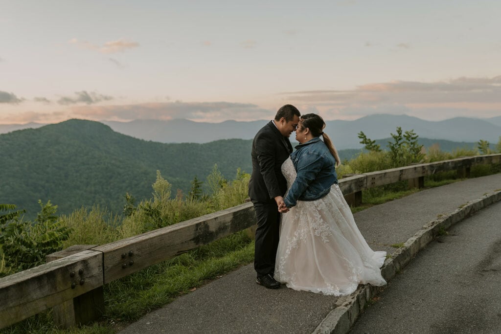 A couple is standing in their wedding clothes, hugging face to face on the Blue Ridge Parkway; one of the best places to elope in NC.