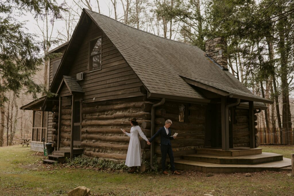 A couple is standing holding hands at the corner of their cabin rental for their Asheville elopement. They are reading letters before their first look.