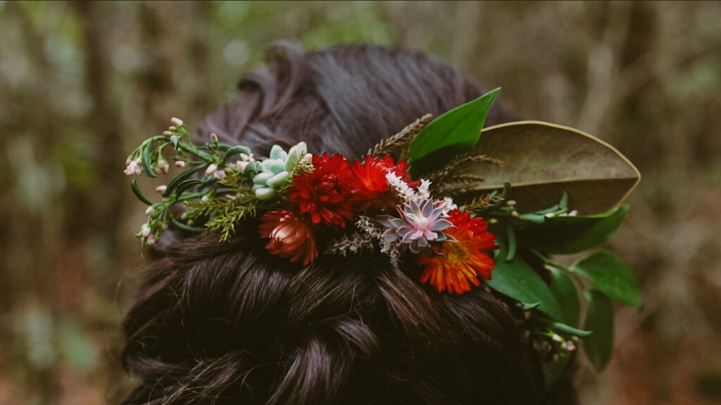 a close up of a hair comb covered in leaves, flowers and succulents places on a up-do dark brown hairstyle.