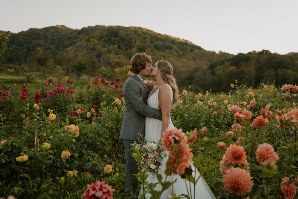 A couple stands kissing during their elopement in a field full of flowers right after sunset.