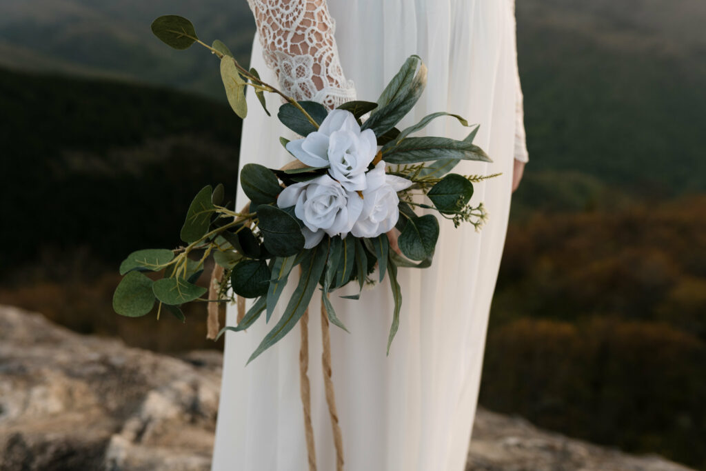 A close up shot of a large floral wristlet a bride is wearing on her elopement day on a mountaintop. It has 3 white flowers and lots of greenery sprays and is made of silk.