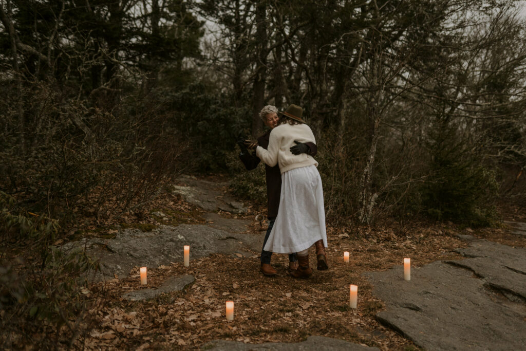 A couple has an outdoor first dance with candles on top of a mountain on an overcast winter day.