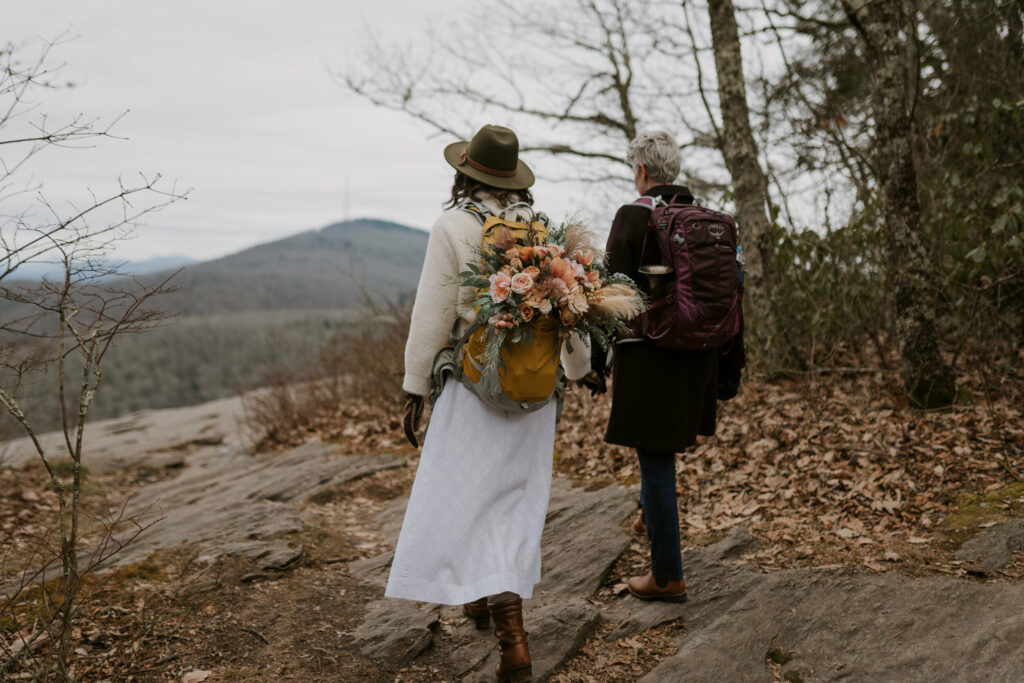 A couple stands walking out to a mountain view with backpacks on during their adventure elopement in western NC.