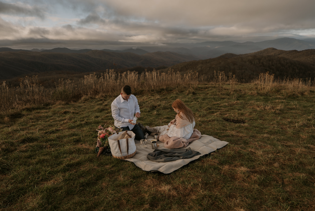 A couple sits on a blanket they packed for a picnic during their adventure elopement. They are having a morning picnic with a mountain view