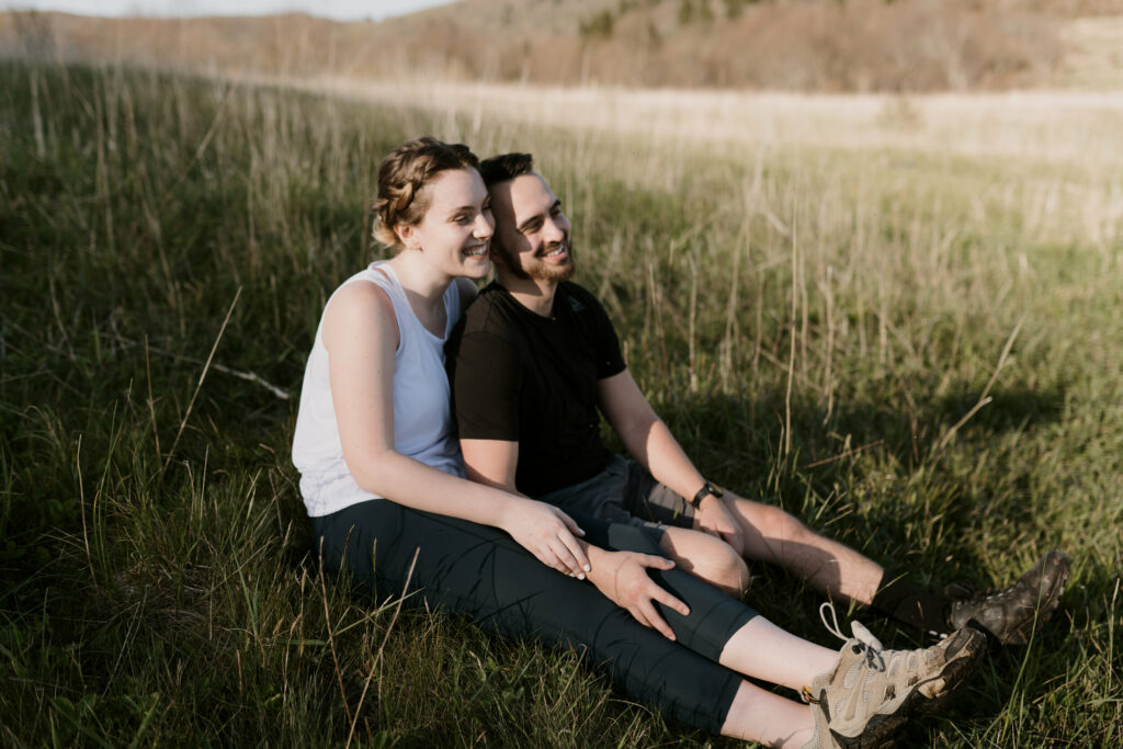 A couple sits side by side in tall grass smiling