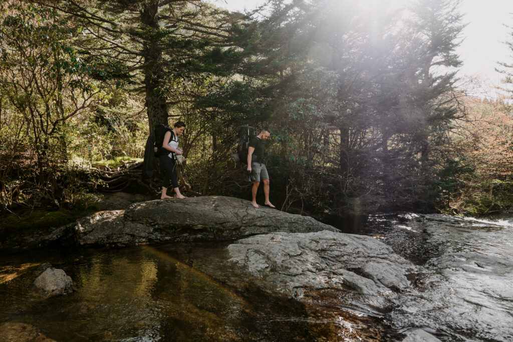 A couple walks down a rock to prepare for a creek crossing during their backpacking elopement in NC.