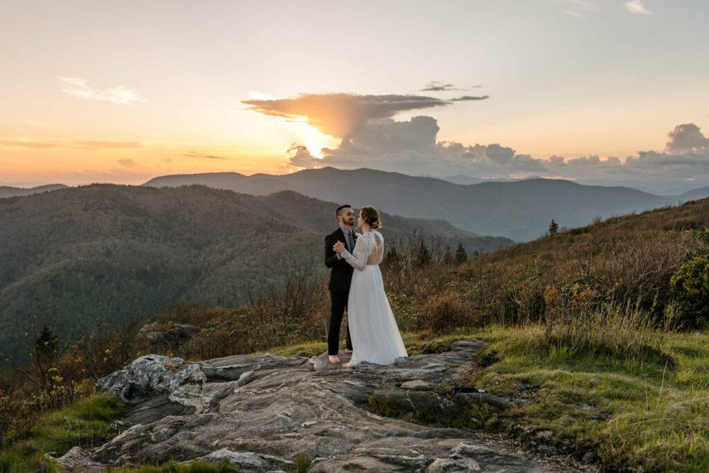 A couple stands in the distance on a mountain in NC for their elopements first dance at sunset.