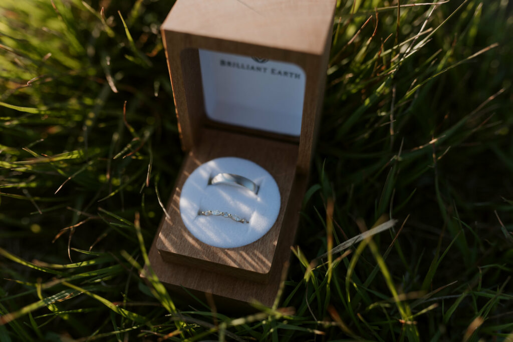 A ring box with the bride and grooms ring sit in the grass during a backpacking elopement in NC.