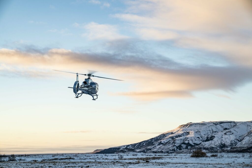 A helicopter flies through the air in a snowy scene at sunset. Helicopter tours are a great idea for an elopement day to get a different view