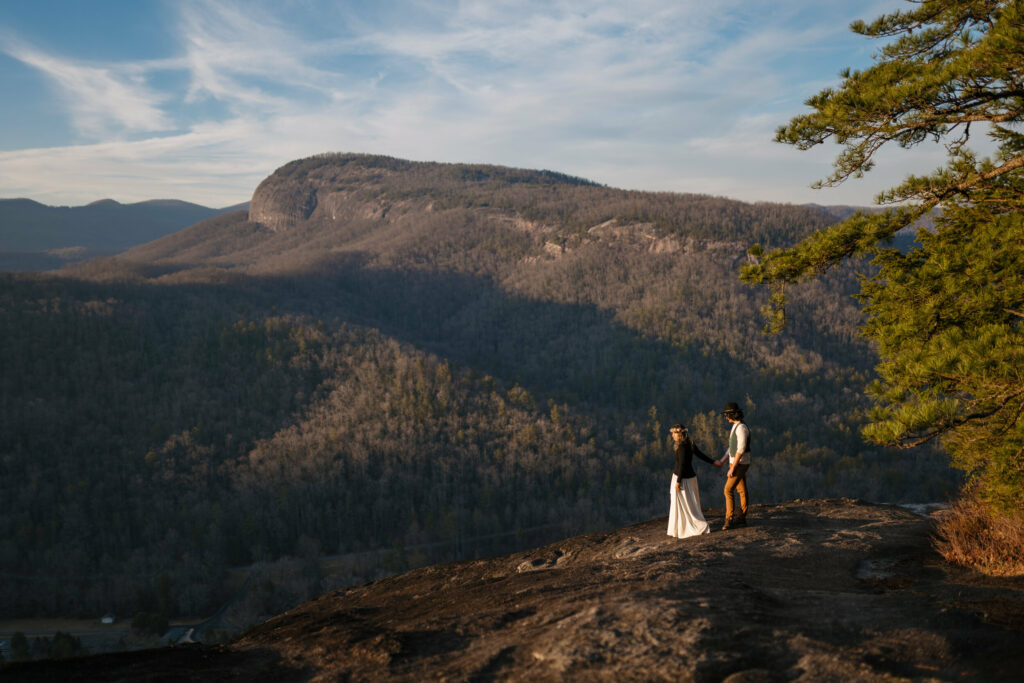 A couple is small amidst a massive mountain landscape during their hiking elopement at sunset.