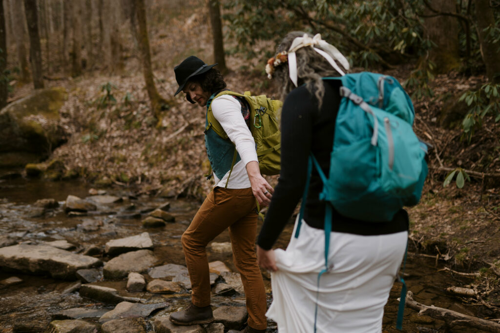 A couple reaches to hold hands while hiking over a river during their elopement day.