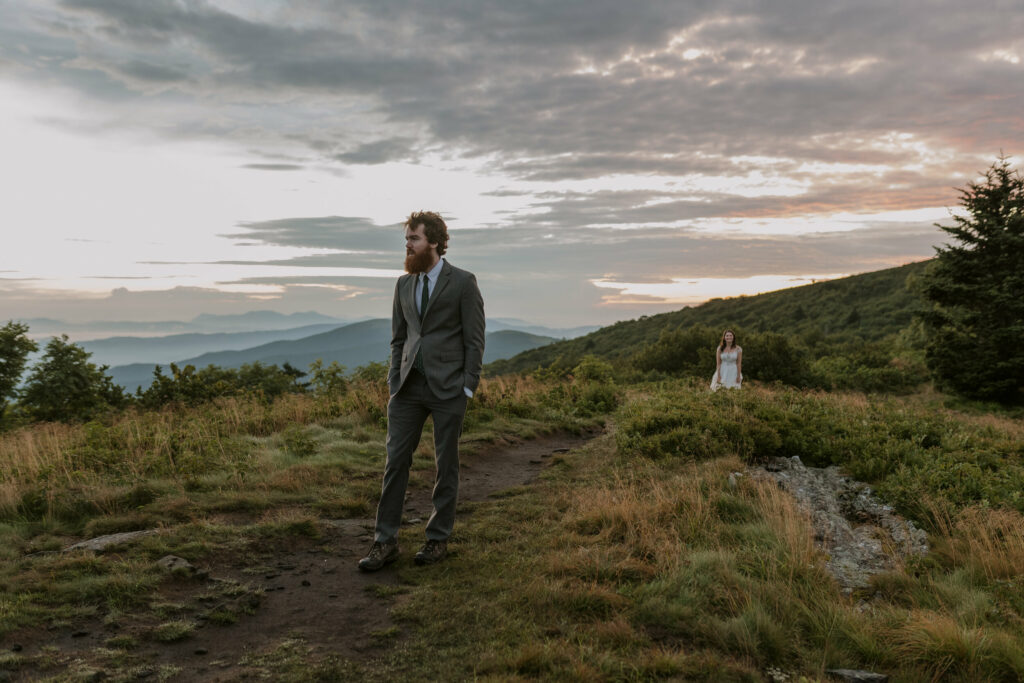 A bride and groom stand feet apart on a mountain for their elopement day, about to have their first look where they see each other in their clothes for the first time. The sun is rising behind them.
