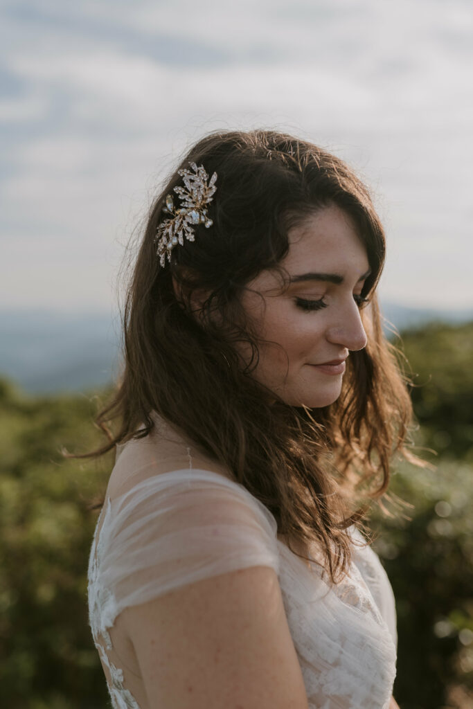 A close up portrait of a bride standing on a mountain with her head tilted down to show a leaf shaped jewelry hairpiece she is wearing for her elopement.
