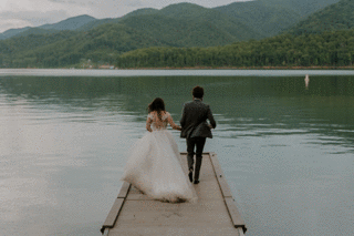 A couple runs and jumps in a mountain lake with their elopement clothing on.