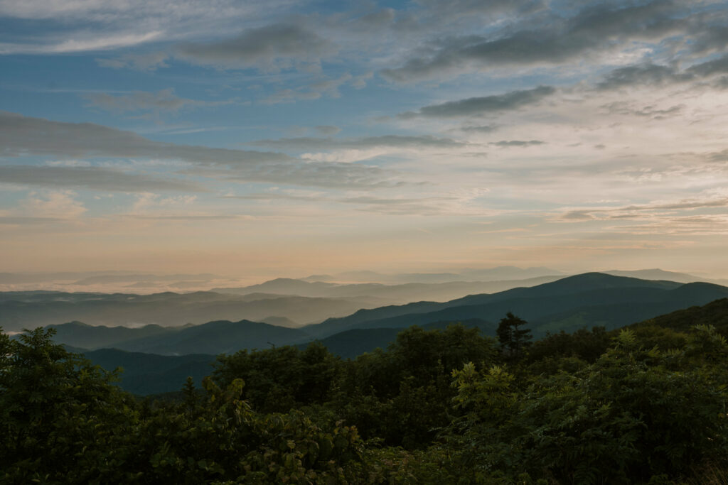 A blue ridge mountain landscape with foggy layers and cloudy skies.