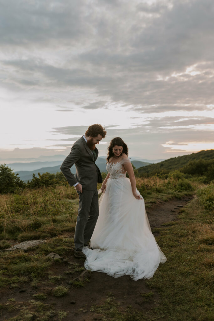 A bride and groom look at the brides wedding dress during their mountain elopement at sunrise.
