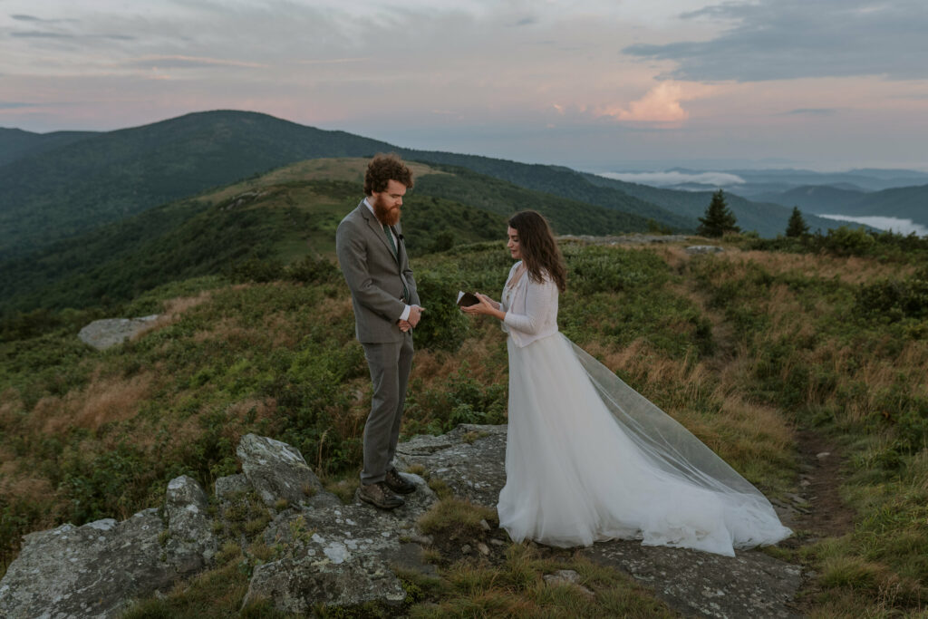A bride is reading out her vows during an elopement on a trail through the blue ridge mountains at sunrise.