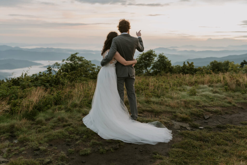 A bride and groom hug each other facing out toward a mountain view during their elopement at sunrise.
