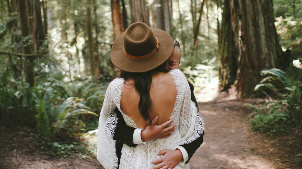 A couple stands in their wedding clothing hugging under the redwood trees during their elopement while feeling very emotional.
