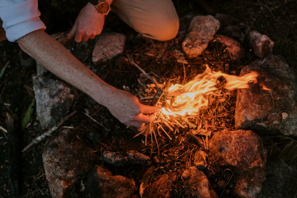 A groom is preparing a bonfire by putting little pieces of wood on top of the flames.
