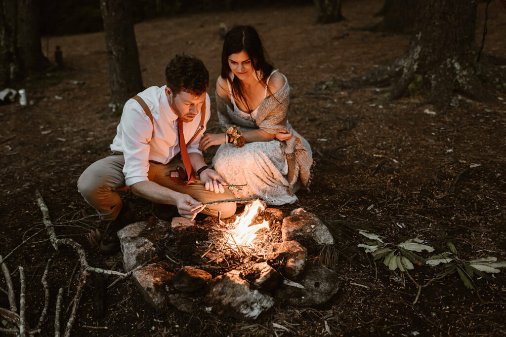 A couple is making a campfire during their elopement in the forest of NC surrounded by pine nettles and trees.