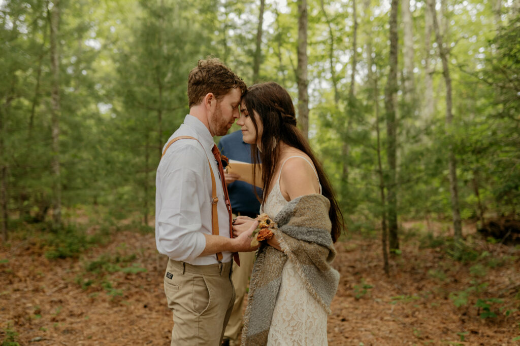 A bride and groom are standing forehead to forehead during their ceremony for their elopement in a North Carolina forest.
