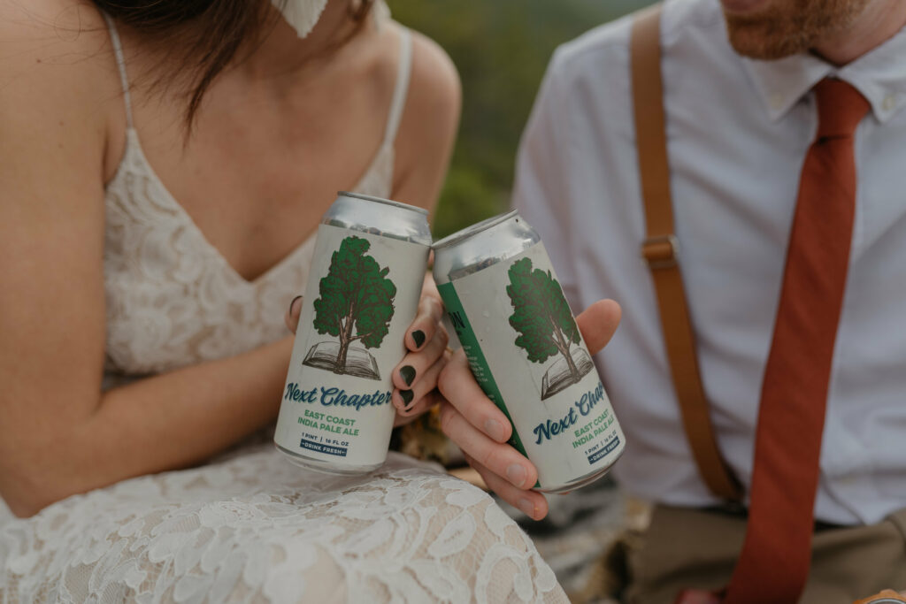 An up close image of a couple on their elopement day holding beers called “next chapter".