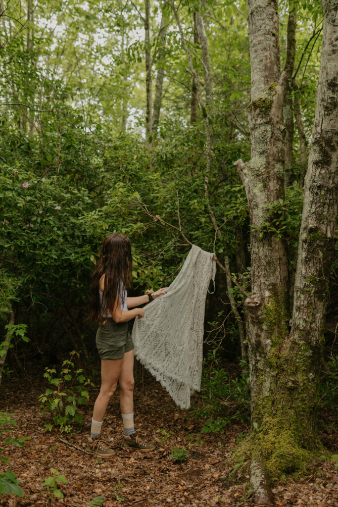 A bride is hanging up her wedding dress on a tree limb in a forest, about to get ready for her elopement in North Carolina.