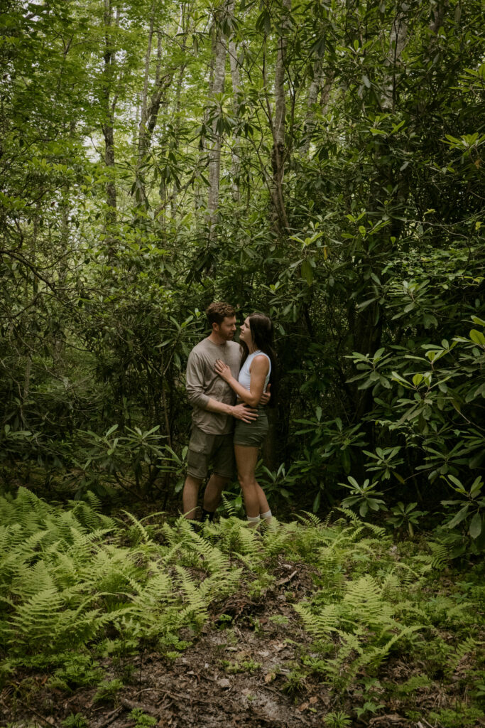 A couple is standing in a forest surrounded by trees and ferns during their North Carolina elopement.