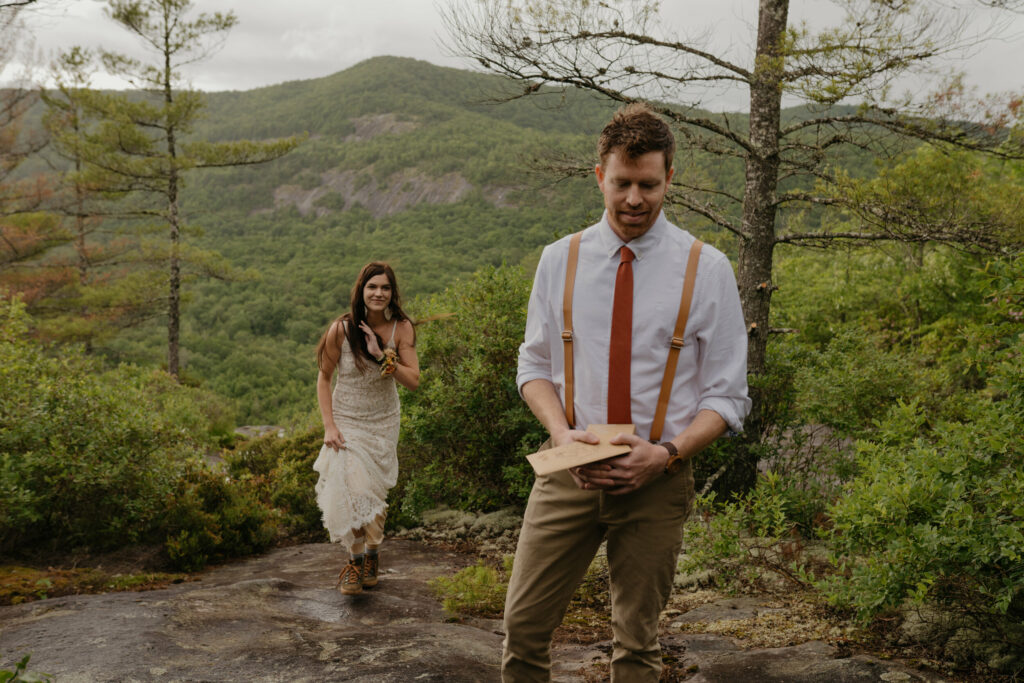 A bride is walking up to her groom during their elopement in North Carolina surrounded by forest in the summer. They are about to have their first look, so the groom is waiting to turn around.