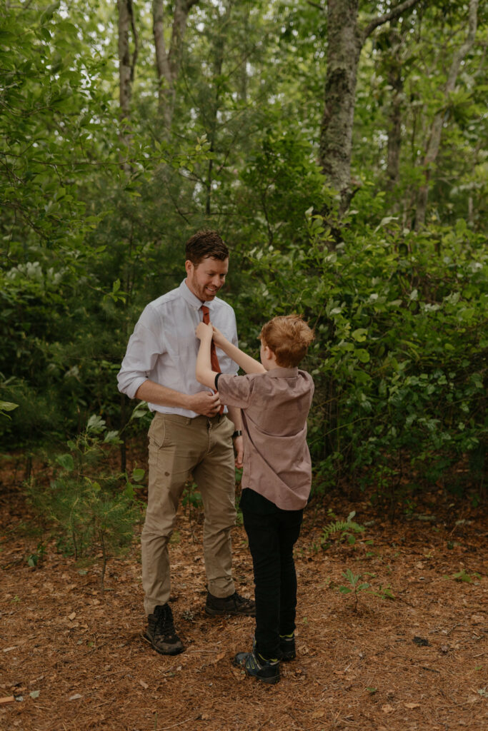 A son is helping tie his fathers tie in a forest in North Carolina during his fathers elopement day.