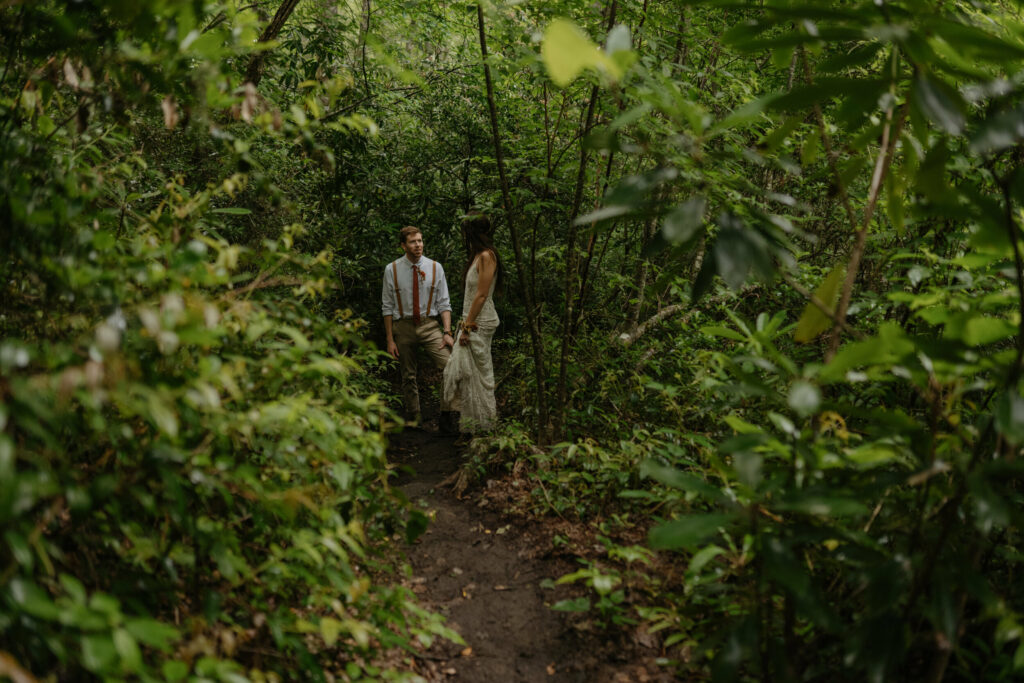 A couple is hiking through the forest in North Carolina during their elopement day. They are taking a break down the trail.