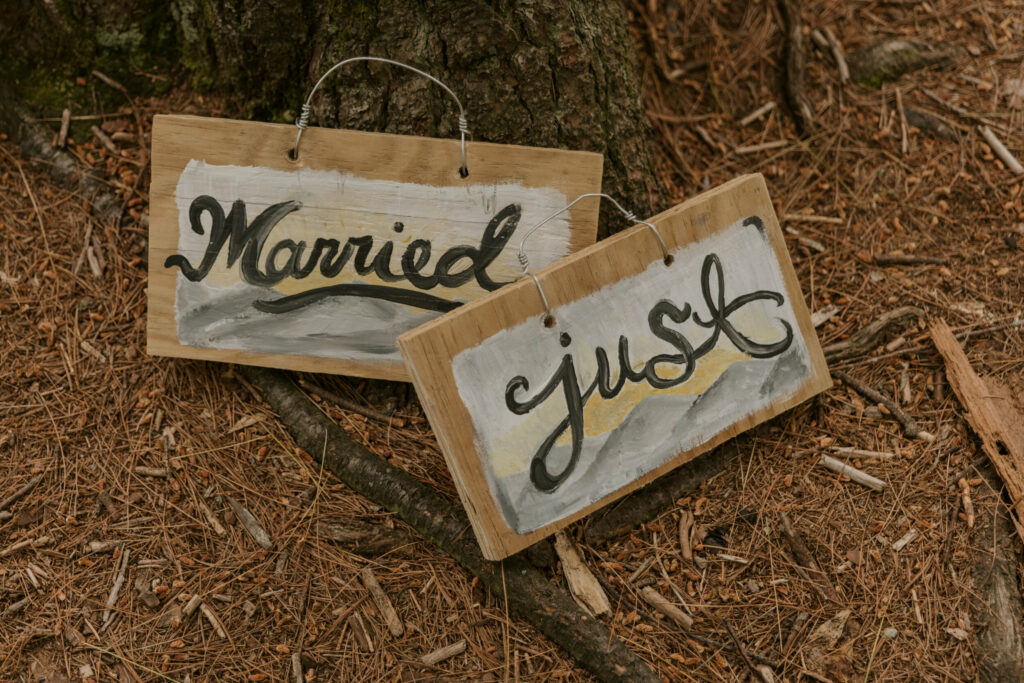 Two hand painted signs that read “just married” when paired together lie against a tree.