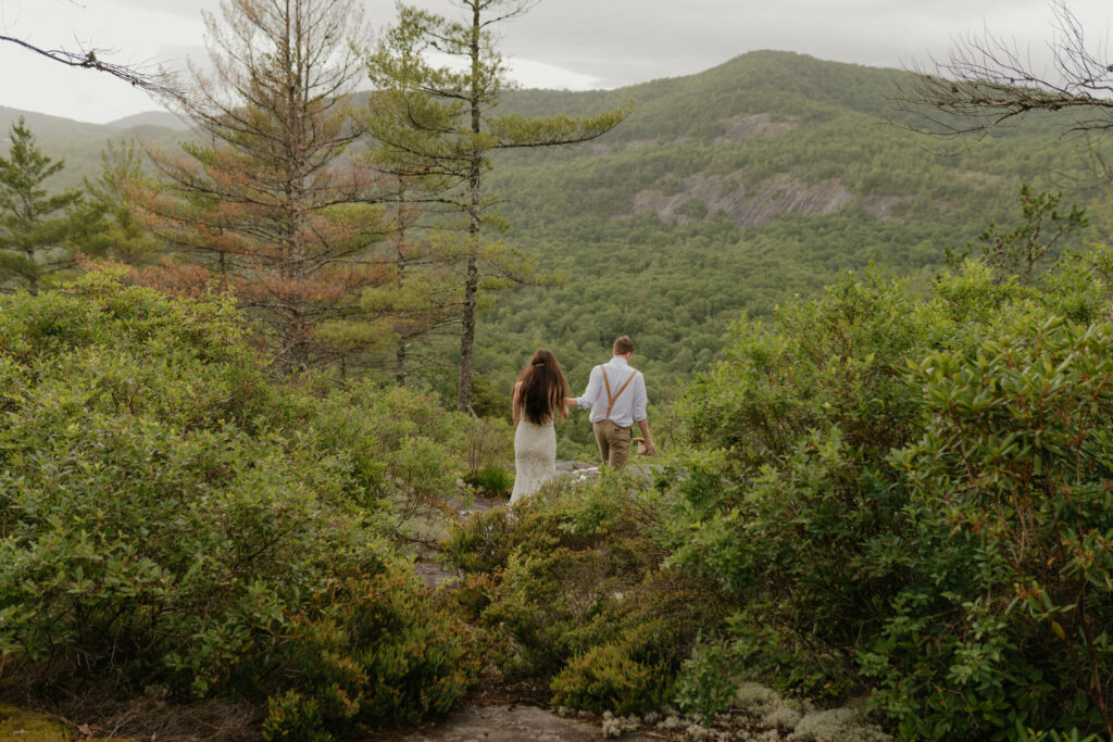 A couple is walking through the forest hand in hand during their North Carolina elopement.