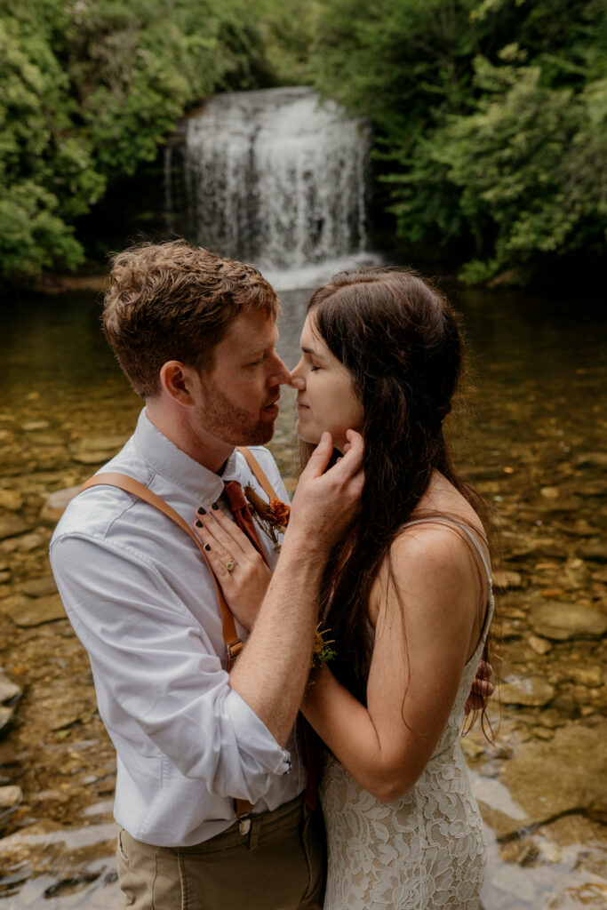 A couple is kissing on a rock in the river by a waterfall in North Carolina on their elopement day.