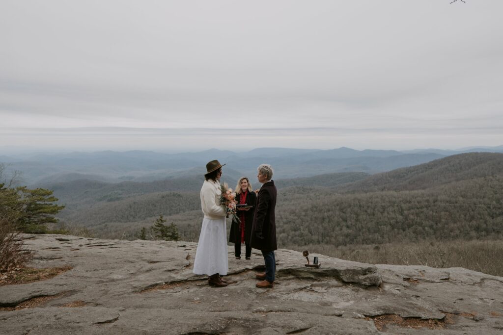 A couple stands in front of their officiant with a winter mountain scene behind them during the ceremony of their blue ridge parkway wedding.