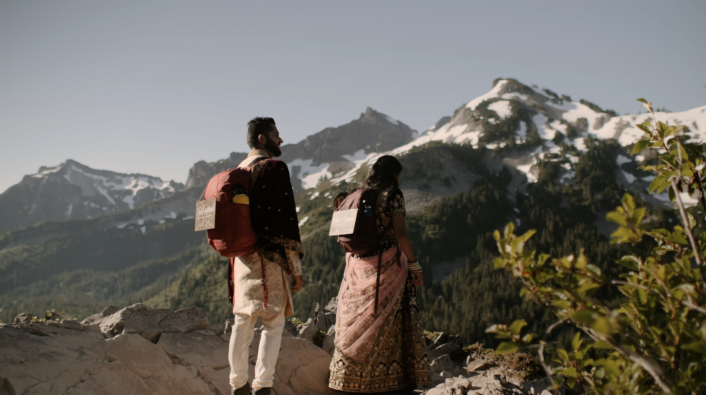 A couple eloping in Washington state are hiking up to a viewpoint with snow covered mountains in their traditional Indian wedding attire.