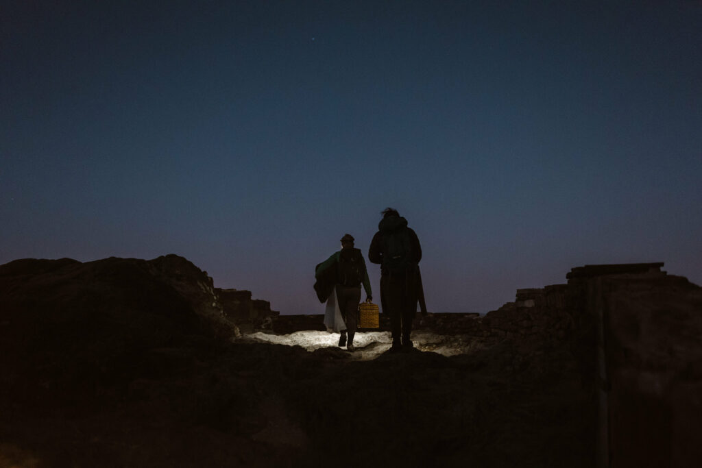 A couple hikes up a mountain the dark wearing wedding clothes to their intimate sunrise wedding.