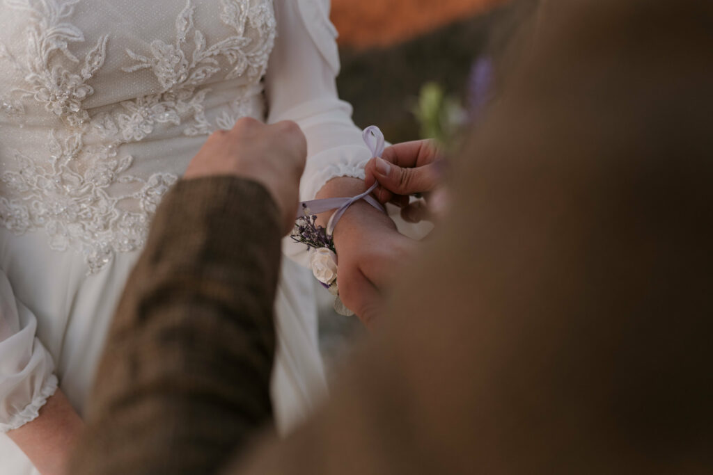 Husband ties corsage on the wrist of his wife at their intimate sunrise wedding.