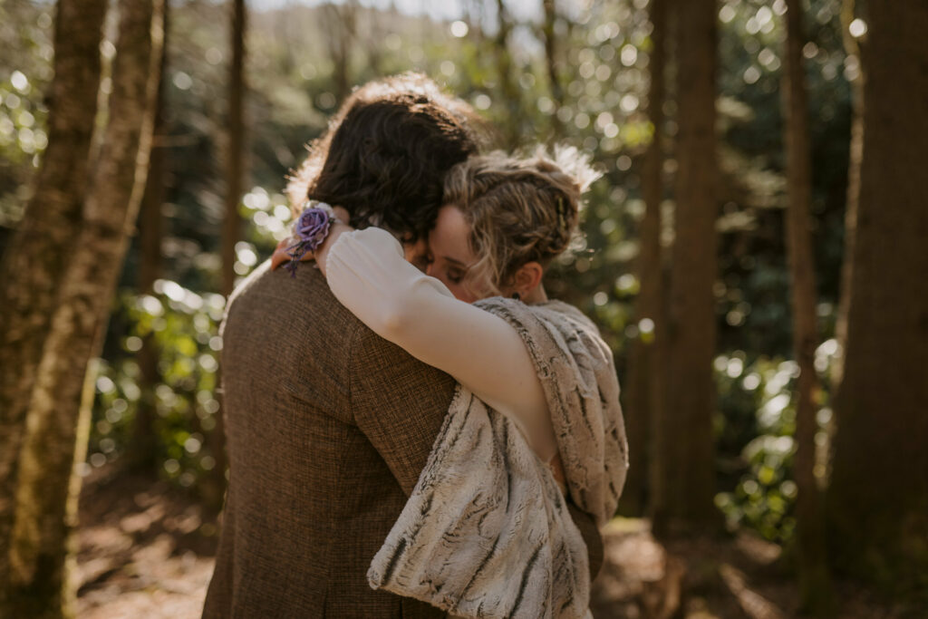 A newlywed couple hug during their first dance as husband and wife in the woods during their intimate sunrise wedding.
