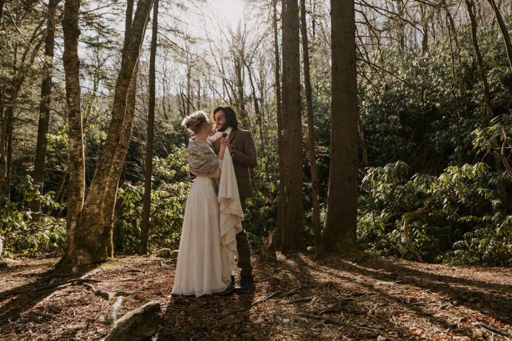 Man and woman wearing wedding clothes dancing in the forest during their intimate sunrise wedding.