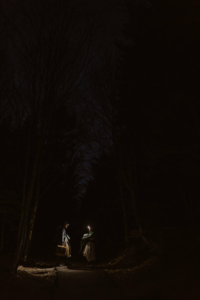 A couple stands in the dark wearing headlamps.