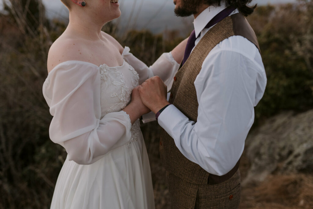 Close-up of a man and woman holding hands on top of a mountain before their elopement.