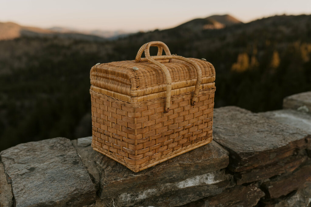 A picnic basket sits on the edge of an overlook in the mountains.