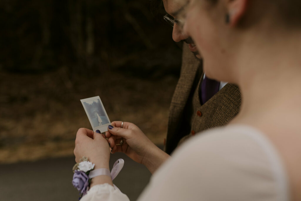 A woman in a wedding gown looks at a polaroid of herself and her husband during their intimate sunrise wedding.