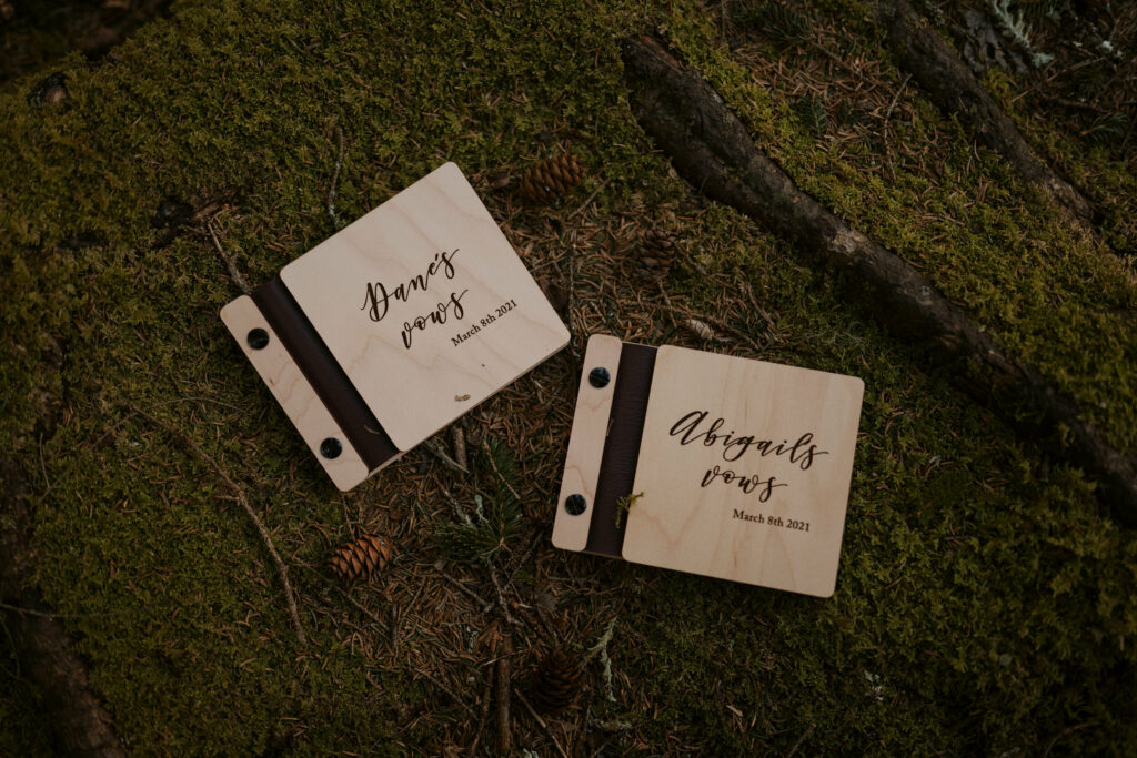 Two wooden vow books sit on a bed of moss during a couple's intimate sunrise wedding.