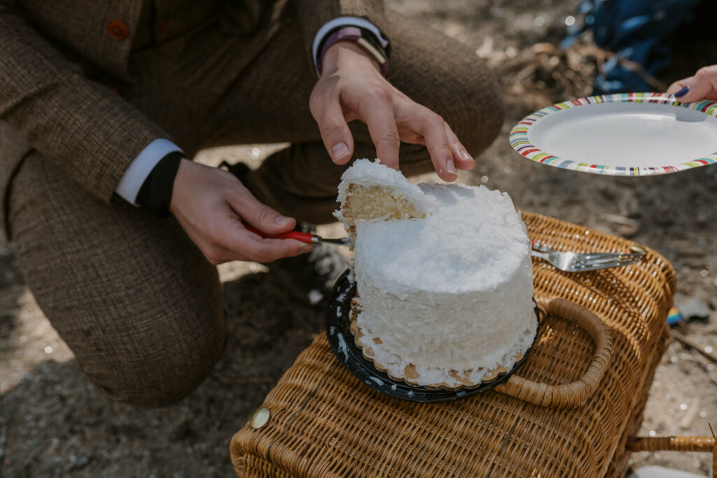 A closeup of a man cutting a small white wedding cake.