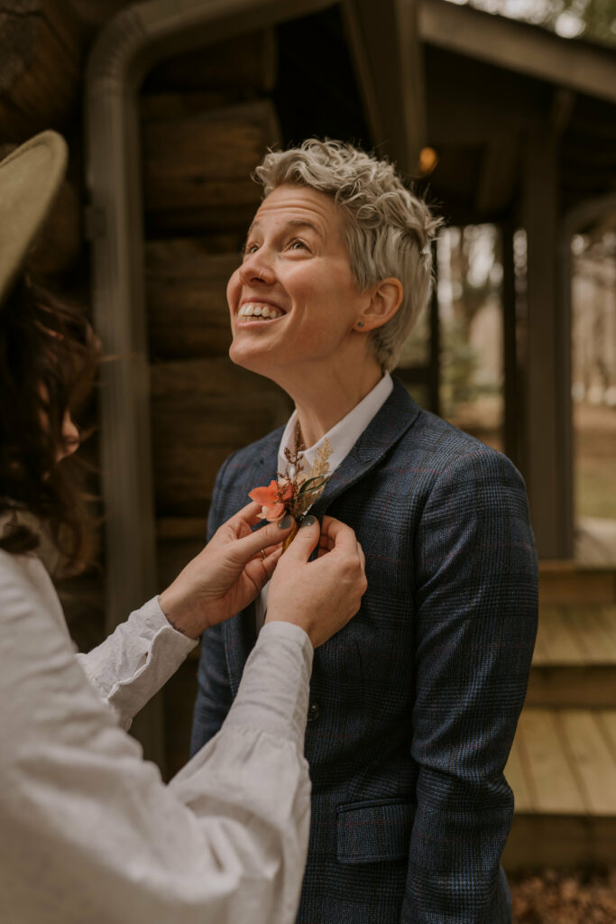 A woman pins a boutonniere on her partner before their elopement.