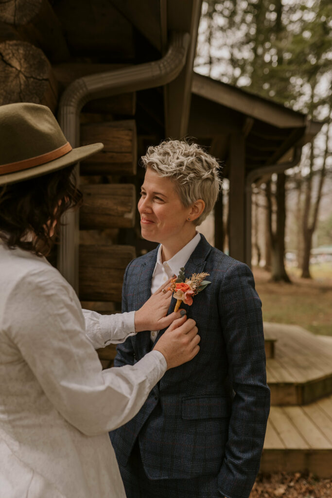 A woman fixes the boutonniere placement on her partner’s suit before their wedding.